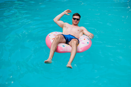 A cute man in shorts swims in the pool on an inflatable ring. Summer vacation in the pool of a single man.