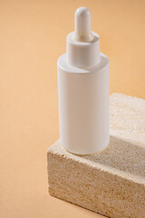 Serum in glass bottle with dropper lid on natural sandstone. Essential oil for care of women's skin on beige background, anti age cosmetics presentation