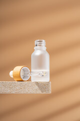 Mock-up of matte glass bottle with dropper lid on natural stone shelf. Facial serum, essential oil for care of women's skin on beige background, mockup