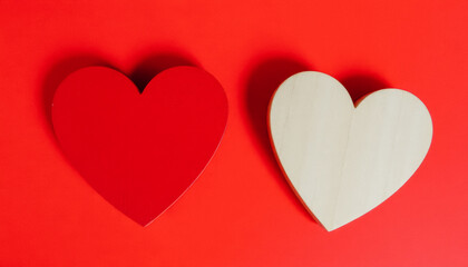Two wooden hearts, one red and one natural, placed on a red background, symbolizing love and unity for Valentine's Day.