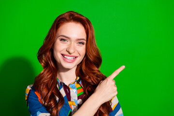 Smiling young woman with colorful style pointing against vibrant green backdrop for advertising or...
