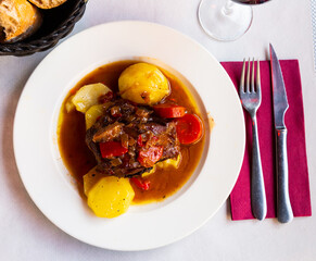Baked lamb shoulder with vegetables and sauce served on white plate