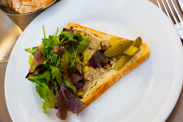 Piece of traditional French Pate en croute maison served on white plate with pickled cucumber and mix of greens