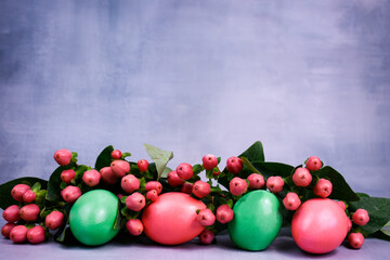Bright Easter eggs of pink and green colors in a festive composition with hypericum sprigs on a light wooden background.