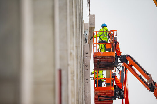 Construction workers working on large scale telescopic boom lift platforms for massive warehouse and factory building. Industrial big lift platforms helping construction business to grow