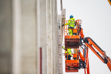 Construction workers working on large scale telescopic boom lift platforms for massive warehouse...