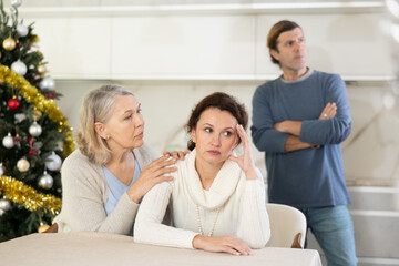 Obraz premium On Christmas Eve woman sits near daughter and comforts during quarrel with husband. Mother calms upset daughter takes side of woman in altercation with brother. Man is outraged by girlfriend behavior