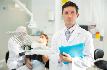 Adult male nurse taking notes while examining patient in dental office