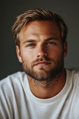Fototapeta premium Man with tousled hair and expressive blue eyes wearing a casual white shirt, posing indoors with a contemplative expression