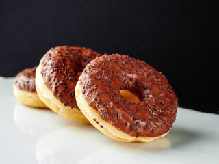 Three chocolate donut with sprinkles on top. The donut is sitting on a white surface and dark background. Premium high quality bakery product.