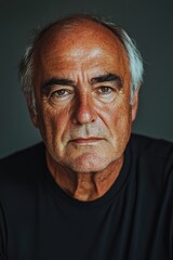 Fototapeta premium Senior man with gray hair displays a contemplative expression against a dark background in a dimly lit setting