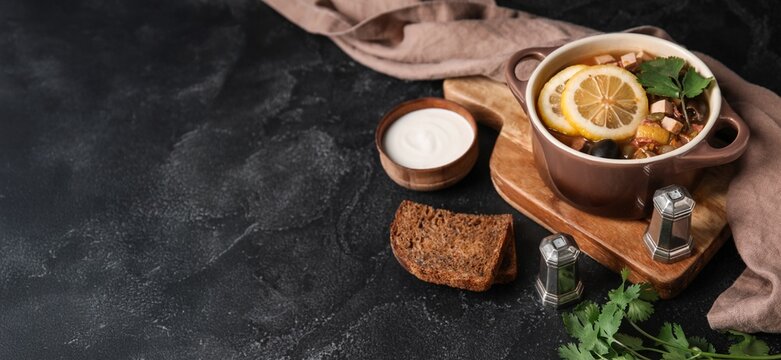 Bowl of tasty hodgepodge soup, spices, bread and sour cream on dark background with space for text