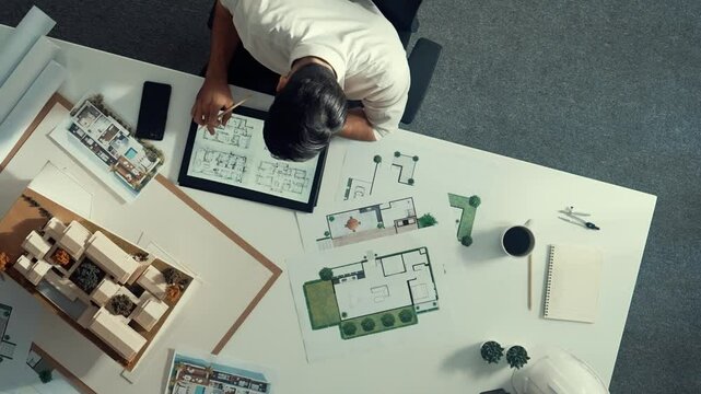 Top view of business man using tablet plan house design while sitting at meeting table with blueprint and equipment scatter around. Aerial view of civil engineer working at blueprint. Alimentation.