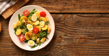 Plate of tasty potato salad with eggs and tomatoes on wooden background, top view
