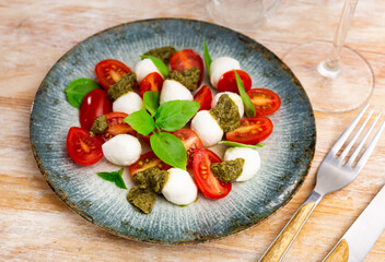 Italian salad, caprese with basil leaves and pesto sauce, served on table.