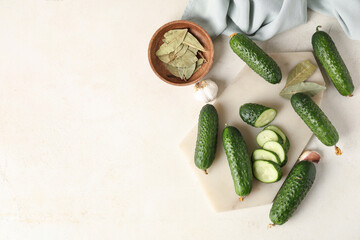 Board of fresh green cucumbers and wooden bowl with bay leaves on white background