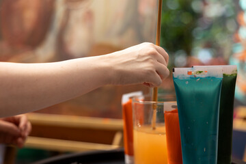 Talented artist using watercolor paint tubes to create an artwork on canvas, using artistic supplies and brushes to paint a beautiful masterpiece. Painter with creativity and inspiration. Close up.