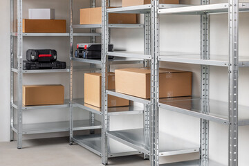 Metal warehouse shelves filled with different sizes of beige cardboard boxes and black plastic tool boxes. Storage concept