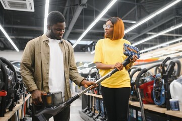 African american couple crouching and looking at vacuum cleaner they want to buy. Tech store interior.