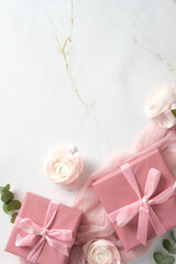 Pink gift boxes with rose ranunculus flowers and eucalyptus on marble background. Romantic flat lay composition. Happy Mothers Day, International womens day, birthday concept.
