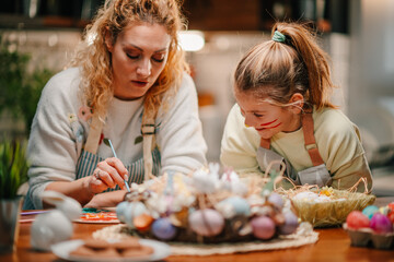 Mother and daughter painting easter eggs at home