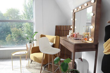 Wooden dressing table with cosmetics, accessories, chair and armchair near light wall in room