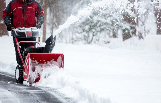 A person operating a snow blower to clear a driveway