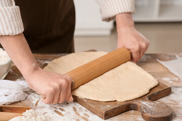 Woman rolling out fresh dough in kitchen