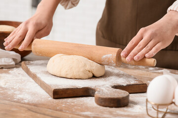 Woman rolling out fresh dough in kitchen