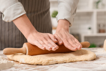 Woman rolling out fresh dough in kitchen