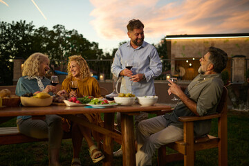 Group of mature friends enjoying food and drinks at backyard party