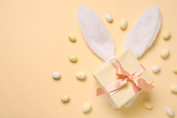 Bunny ears with Easter eggs and gift box on beige background