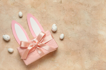 Paper bunny ears with Easter eggs and gift box on beige grunge background