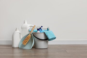 Bucket with cleaning products and dustpan on laminate floor against white wall