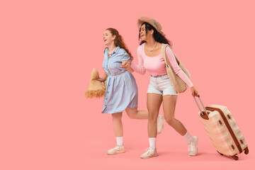 Beautiful young happy female friends with summer bags and suitcase on pink background