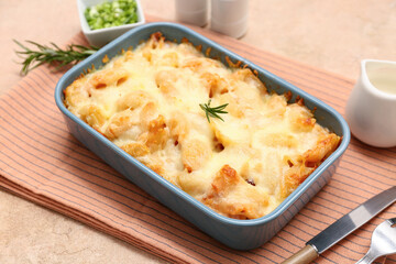 Baking dish with tasty pasta, rosemary and cheese on beige grunge background