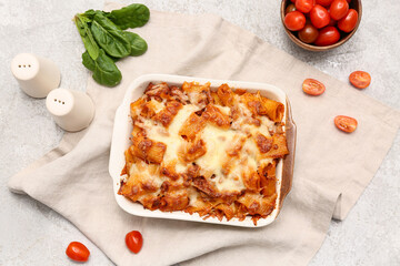 Baking dish with tasty pasta, tomatoes and spinach leaves on grey grunge background