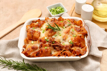 Baking dish with tasty pasta, rosemary and cut green onion on beige grunge background