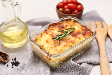 Baking dish with tasty pasta, rosemary, peppercorns and jug of oil on light background