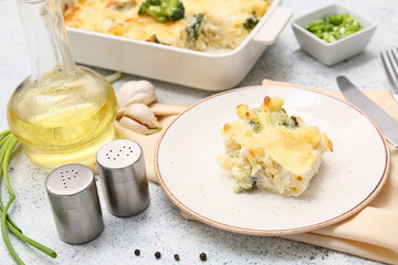 Plate with tasty baked pasta, broccoli, green onion, garlic and jug of oil on light background