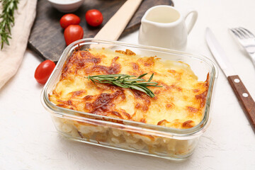Baking dish with tasty pasta, rosemary, tomatoes and jug of milk on white background