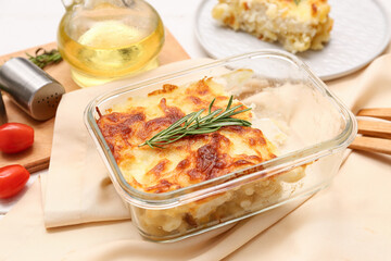 Baking dish with tasty pasta, cheese and rosemary on napkin