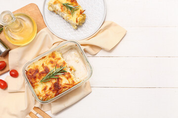 Tasty baked pasta with rosemary, tomatoes and jug of oil on white wooden background