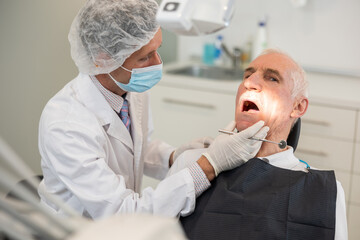 Mature man is sitting in armchair during dental diagnosis at dentist appointment. Male doctor...
