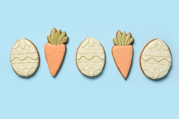 Composition with Easter cookies in shape of carrots and eggs on blue background