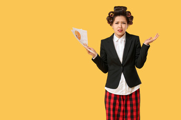 Displeased Asian businesswoman with hair curlers and papers on yellow background