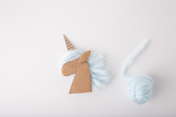 Top view of carton unicorn head with light blue yarn ball on right side. White background, soft...
