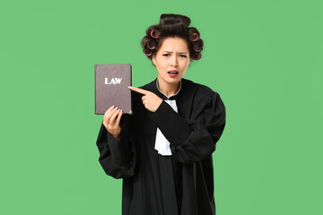 Female Asian judge with hair curlers pointing at law book on green background