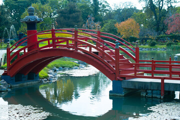 Traditional red Japanese bridge over a pond, surrounded by lush greenery, in Buenos Aires' Japanese Garden.