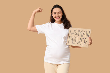 Young pregnant woman with placard showing muscles on beige background